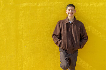 Happy guy smiling looking at camera. Yellow wall background. Latin 18-20 years old guy. Outdoor portrait