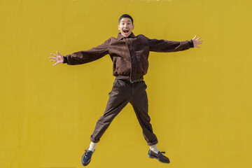 Fototapeta na wymiar Cheerful guy jumping with opened arms. Yellow wall background. Latin 18-20 years old guy. Outdoor portrait.