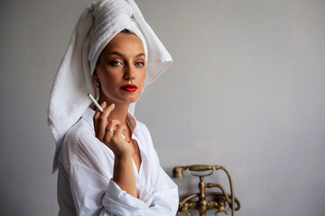 Portrait of beautiful young woman with turban towel on head standing at grey wall