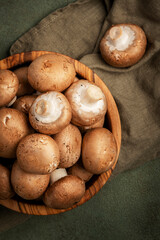 Raw brown champignon mushrooms in wooden olive bowl, old rusty green kitchen table, top view, negative space