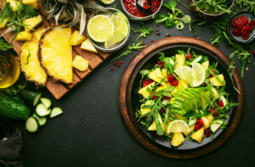 Vegan vegetarian salad with pineapple, arugula, avocado and dried cherry on black plate on dark stone kitchen table, top view. Healthy eating, clean diet food, weight loss concept