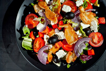 Salad with tomatoes, peppers, olives and chicken fillet. Fresh salad in a black plate on a dark...