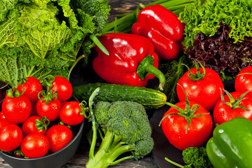 Cabbage, peppers, tomatoes, cucumbers, lettuce, cherry tomatoes, broccoli, arugula on a black background. variety of vegetables on a pile on a wooden table.
