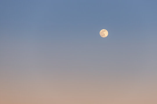 Scenic beautiful abstract full moon against clear blue to orange warm cold sunset or sunrise sky pastel background. Moonlight at evening or morning summer twilight time