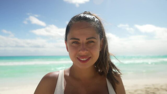 Happy young woman standing at Cancun Beach. Sensuous female with windswept hair is looking at the camera. She is wearing white bikini top during summer vacation at Cancun Mexico.