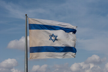 A large, blue and white flag of the State of Israel rippling in the wind on a sunny day during the national observance of the Independence and Memorial day holidays.