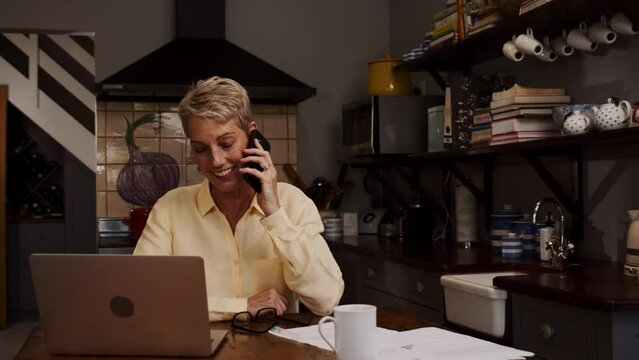 Caucasian elderly women working from home chatting on cellular device 