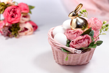one golden rabbit in basket behind white background with flowers and 3 eggs