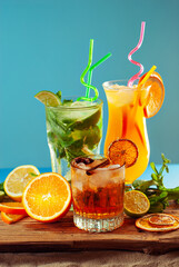 Orange and green cocktails on a wooden board. Alcoholic drink with ice, orange, mint and lime on the sand. A mixture of different drinks with fruit.