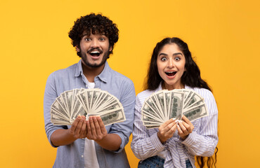Emotional indian man and woman holding bunch of money banknotes, won lottery, showing prize at...