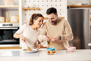 A happy couple in the kitchen preparing eggs for breakfast in their cozy apartment.