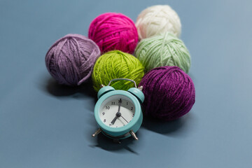 Fototapeta na wymiar Alarm clock next to balls of wool on a blue background. Time to knit