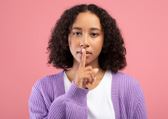 Shh, keep silence, confidential information. Young African American woman gesturing hush on pink...