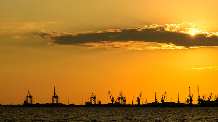 View of cranes in the Thessaloniki cargo port against a cloudy sky in the sunset. Greece