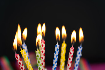 Many burning colorful birthday candles, black background with copy space