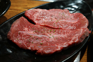 Red raw meat is served on a black plate.
