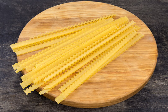 Uncooked long mafaldine pasta on a round wooden board