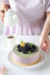 Coconut cheesecake with Japanese matcha tea and white chocolate and berries on a light table. The girl's hands are holding the kettle.