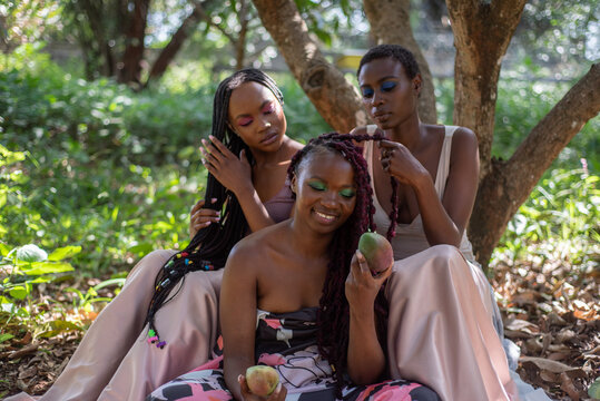 Portrait of three young African women seated in a mango orchard