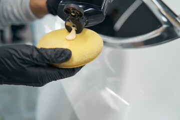 Gloved hands applying liquid wax on foam sponge - obrazy, fototapety, plakaty