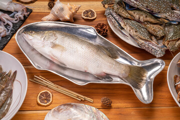 Fresh Sea bass on a fish-shaped plate,  White striped bass fish on wooden background ready to cook.