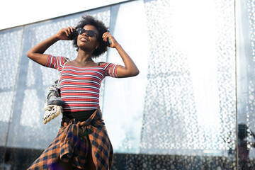 Obraz premium Beautiful African woman with roller skates. Urban sexy girl sitting on the stairs listening the music.