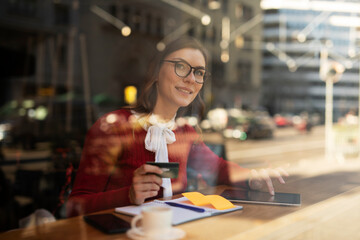 Happy woman using credit card to shopping online with tablet. Beautiful young woman drinking coffee in cafe..