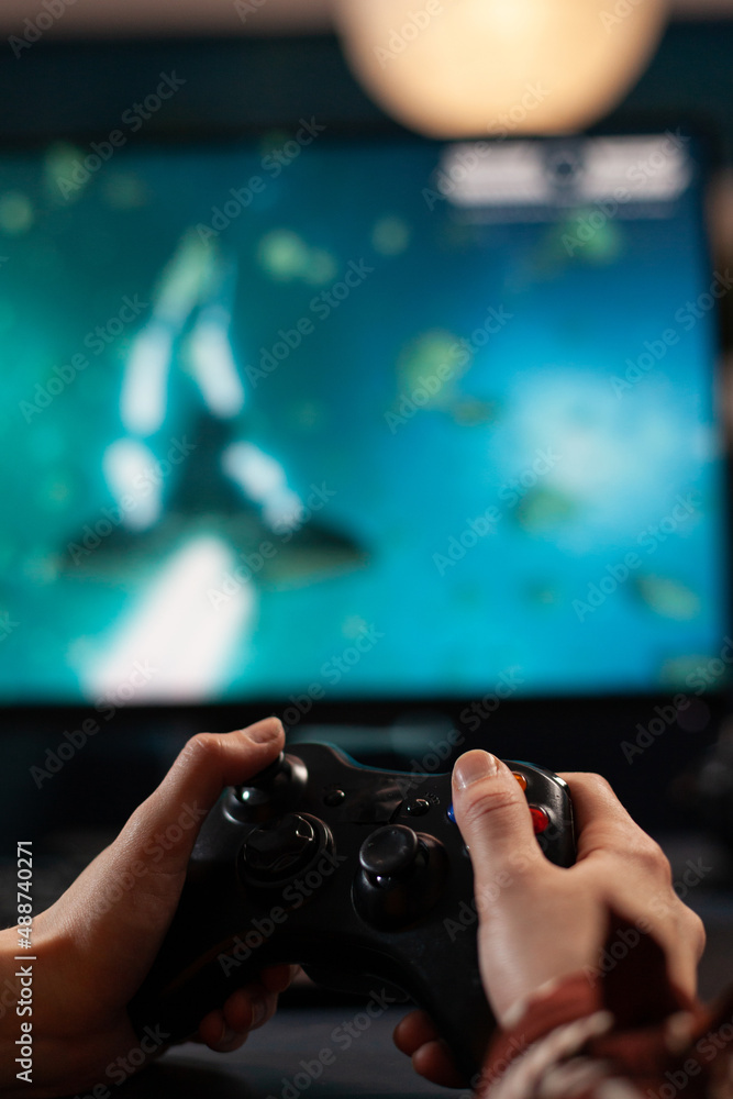 Wall mural Close up of woman holding joystick and playing video games on computer. Gamer using controller to play online digital games in front of monitor. Person with modern gaming equipment