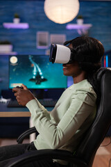 Concentrated african american streamer woman wearing virtual reality headset playing space shooter videogames using gaming controller during online tournament. RGB computer equipment. Cyber space