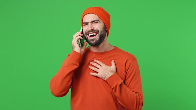 Happy calm smiling fun marvelous young brunet man 20s years old wears red shirt hat hold use talk on mobile cell phone conducting pleasant conversation isolated on plain light green background studio