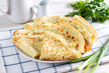 A stack of pancakes with fresh dill and onions on a white plate. Traditional Russian pancakes for Maslenitsa.