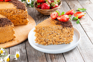 An appetizing piece of waffle cake with condensed milk, chocolate and strawberries on a wooden table. Close up view. Bakery food photography.