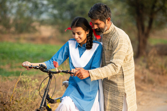 Rural indian father teaching his daughter to ride bicycle at village, young girl wearing school uniform learning cycling. - Powered by Adobe