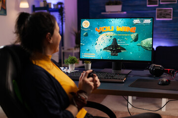 Gamer using controller to play video games on computer. Happy woman winning online games with joystick in front of monitor. Person feeling cheerful and celebrating win on internet. © DC Studio