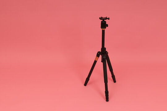 black tripod for camera on pink background with copy space