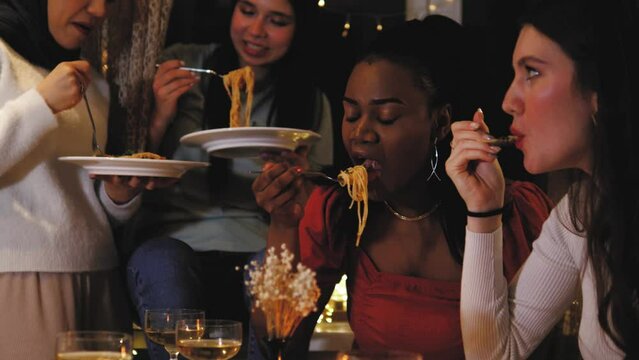 Women friends people eating pasta at dinner together, prepared tasty chilli pasta. Diverse female friends eating meal, having conversation at night