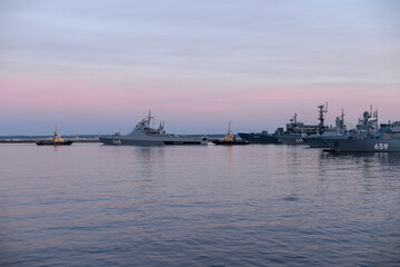 Fototapeta premium Two naval harbor tugs against the background of warships in the Petrovskaya pier of Kronstadt. Evening sunset. Russia, Kronstadt, July 26, 2020