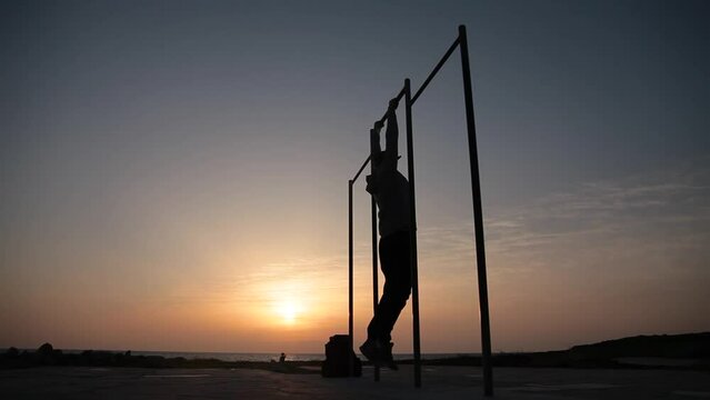Man doing exercises on the crossbar against sunset background. Workout.