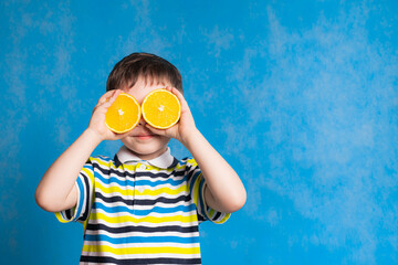 A boy with an orange on a blue background . An article about baby food. Baby vitamins. Copy space.
