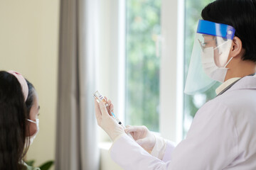 Female doctor in protective mask making a medicine in syringe for vaccination of little patient at...