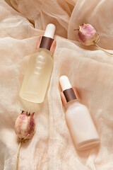 Transparent dropper bottles with essential oil and serum, dried flowers on beige cloth. Aroma oil...