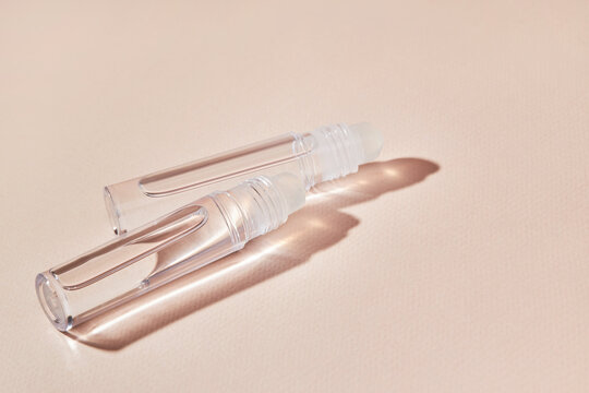 Transparent lip gloss in a roller ball bottles on a beige background. Decorative cosmetic lipstick. Beauty makeup product 