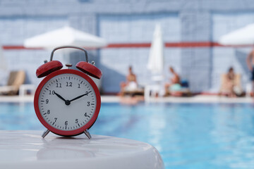 Red alarm clock standing on edge of hotel swimming pool closeup