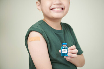 Close-up of little boy with plaster on his arm holding the bottle with medicine in front of him and smiling