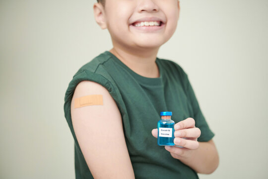Close-up of little boy with plaster on his arm holding the bottle with medicine in front of him and smiling