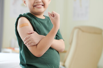 Close-up of brave little boy showing his arm with plaster after vaccination from coronavirus