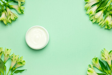 Fototapeta na wymiar Jar of organic cream with flowers on green background. Flat lay, top view, copy space. Natural organic product, beauty and spa concept.