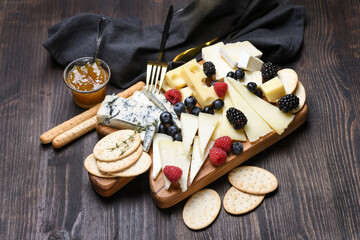 Various types of cheese on a wooden board. Сheese plate  with gorgonzola parmesan brie or camembert and maasdam. served with berries and  crackers 