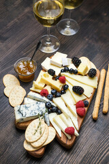 Various types of cheese on a wooden board. Сheese plate  with gorgonzola parmesan brie or camembert and maasdam. served with berries and  crackers 