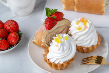 Cakes and sweet roll stuffed with strawberry and cream decorated with strawberries, powdered sugar and mint leaves